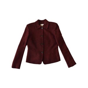 May include: A dark burgundy blazer with a textured, woven fabric finish. The jacket features a classic collar, long sleeves, and a front button closure with four dark buttons. A small white brand label is visible at the inside of the neckline.