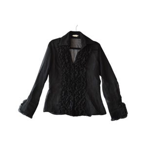 May include: A black long-sleeved shirt made of a sheer, semi-transparent fabric. The shirt features a prominent vertical ruffle detail running down the centre front, a classic collar, and matching ruffled cuffs at the end of each long sleeve.