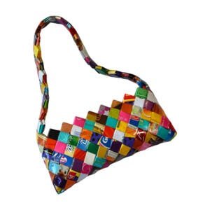 Puede incluir: Un bolso de mano tejido y colorido con un asa curva. El bolso está hecho de pequeños trozos rectangulares de varios colores y patrones, creando un diseño de patchwork. La forma del bolso es triangular, con una base ancha y una parte superior más estrecha.