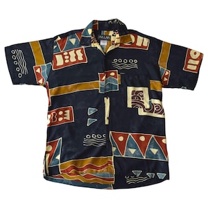 May include: A short-sleeved shirt with a navy blue base and a vibrant geometric design. The pattern features red, yellow, and blue shapes. The shirt has a collared neckline and a chest pocket.