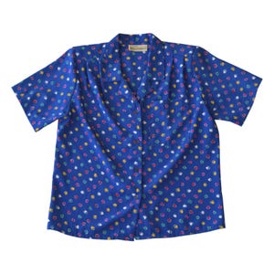 May include: A short-sleeved blue blouse with a colorful polka dot pattern. The blouse has a collared neckline and a button-down front. The polka dots are in various colors, including red, yellow, green, and white.