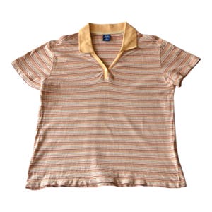 May include: A striped polo shirt in shades of beige, orange, and brown. It features a light yellow collar and a V-neck with a single button. The short-sleeved shirt is made of a soft, lightweight fabric. The shirt has horizontal stripes.