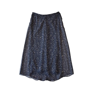 May include: A dark navy blue midi skirt featuring a repeating pattern of small, light-colored, leaf-like shapes scattered across the fabric. The skirt has a high waistline, a flared A-line silhouette, and a slightly curved hemline at the bottom.