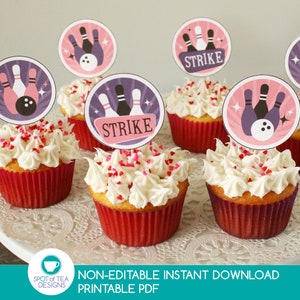 May include: A set of six cupcakes decorated with white frosting and pink sprinkles. Each cupcake has a round, pink and purple themed cupcake topper with a bowling pin design and the word "STRIKE" printed on it.