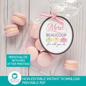 May include: A printable gift tag with the text "Merci Beaucoup for all you do" in a circle with three colorful macarons. The tag is printed on white cardstock and has a black border. The tag is tied with a pink ribbon.