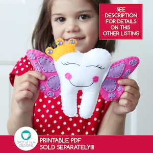 May include: A white felt tooth with a pink and purple butterfly design and a yellow crown. The tooth has a smiling face with closed eyes. The tooth is being held by a child.