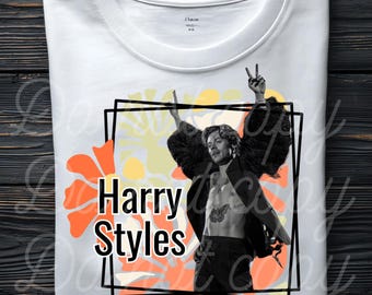 May include: White crew neck t-shirt featuring a graphic of Harry Styles with a floral background. The design includes the text "Harry Styles" in a bold font. The image is framed in a black rectangle.