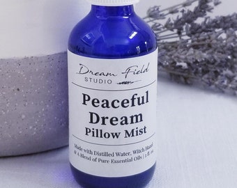May include: A cobalt blue glass bottle of "Peaceful Dream Pillow Mist" with a white label. The label reads "Dream Field Studio" and lists ingredients. A sprig of dried lavender is next to the bottle. The bottle contains 2 fl oz of product.