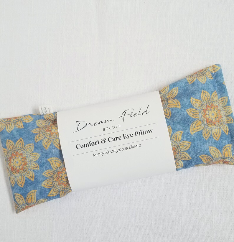 May include: A blue and yellow floral Comfort & Care Eye Pillow from Dream Field Studio. The pillow has a floral pattern and the text "Comfort & Care Eye Pillow" and "Minty Eucalyptus Blend" on the label.