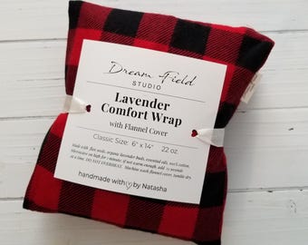 May include: A rectangular lavender comfort wrap with a red and black buffalo plaid flannel cover. A white paper label is wrapped around the center, featuring the text Dream Field Studio, Lavender Comfort Wrap with Flannel Cover, 6" x 14", 22 oz.