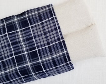 May include: A rectangular fabric pouch featuring a dark navy blue, grey, and white plaid pattern on one side and a plain, unbleached off-white fabric on the other side. The two sections are joined by a visible zigzag stitch along the seam.