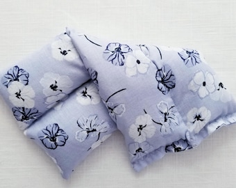 May include: A rectangular fabric heating pad or pillow featuring a light periwinkle blue background with a repeating pattern of white and dark navy blue hand-drawn style flowers. The item is segmented into three distinct sections with visible stitching.