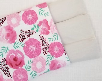 May include: A floral print heating pad featuring a white background with large pink flowers, green leaves, and burgundy accents. The pad is filled with three rectangular sections of a light-colored material.