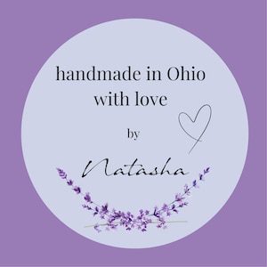 Op de afbeelding: Een ronde, lichtpaarse sticker met de tekst "handmade in Ohio with love by Natasha". Een zwart hart en een lavendel takje zijn ook inbegrepen. De achtergrond is een donkerdere tint paars.