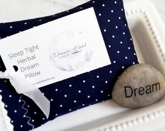 May include: A navy blue polka dot herbal dream pillow with a white tag and a small stone that says "Dream". The tag reads "Sleep Tight Herbal Dream Pillow" and has the Dream Field Studio logo.
