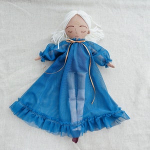 May include: A handmade doll with white hair and a blue sheer dress. The doll has a painted face with closed eyes and a third eye symbol on the forehead.