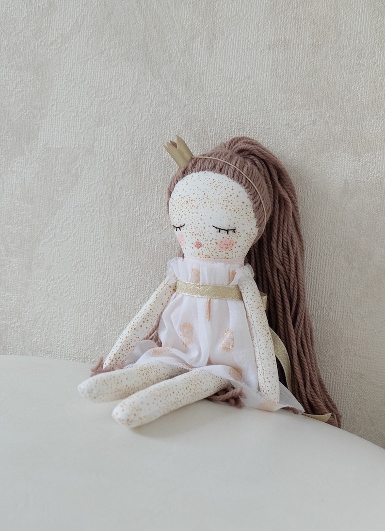 May include: A handmade doll with a white dress, gold trim, and brown yarn hair. The doll is wearing a gold crown and has painted eyes and freckles.