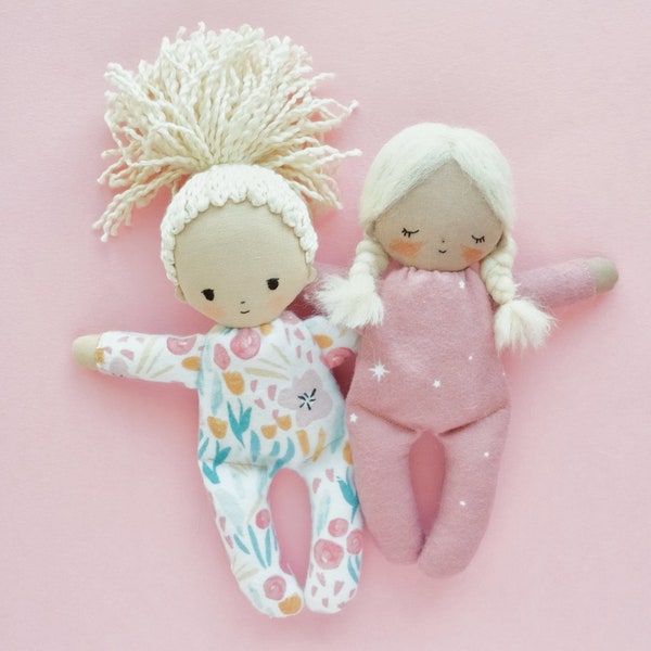 May include: Two handmade fabric dolls with yarn hair. One doll is wearing a pink outfit with white stars and the other doll is wearing a floral print outfit.