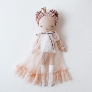 May include: A handmade doll wearing a pink tulle dress with a gold crown. The doll has brown hair and closed eyes.