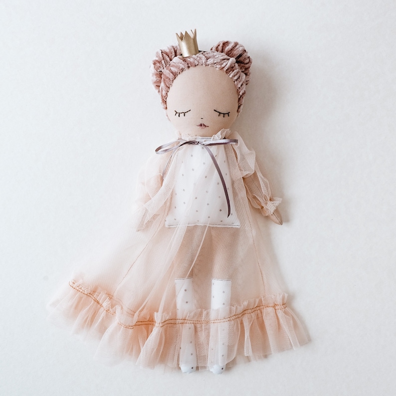 May include: A handmade doll wearing a pink tulle dress with a gold crown. The doll has brown hair and closed eyes.