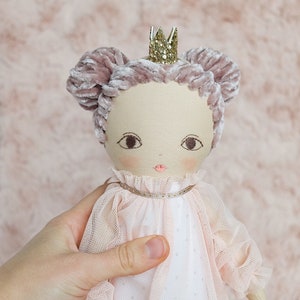 May include: A handmade doll with a pink velvet crown, pink velvet hair, and a white tulle dress. The doll is wearing a gold glitter crown.