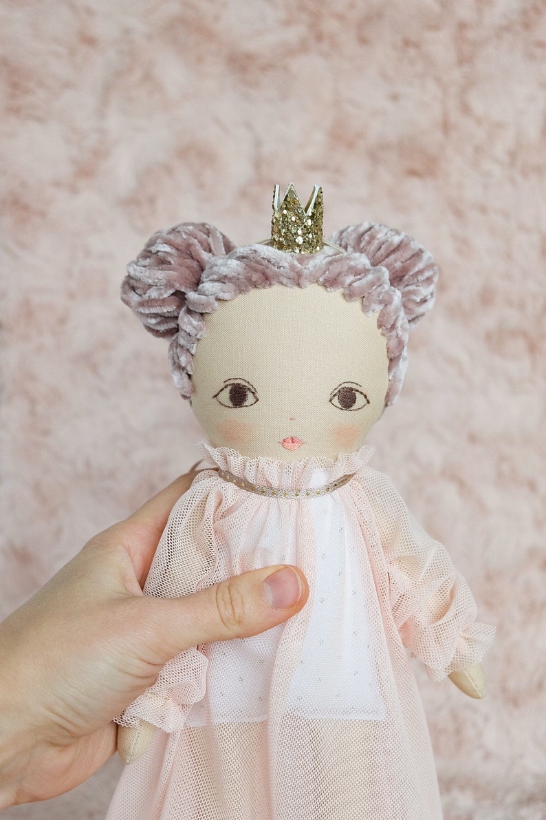 May include: A handmade doll with a pink velvet crown, pink velvet hair, and a white tulle dress. The doll is wearing a gold glitter crown.
