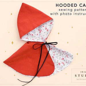 May include: A red hooded cape with a white floral lining and black ties. The cape is laid flat on a light pink background with gold stars. The text "HOODED CAPE sewing pattern with photo instructions" is at the top of the image. The text "10x2 STUDIO by Victoria Zhuk" is at the bottom of the image.