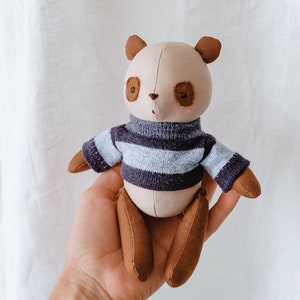 May include: A plush panda bear toy wearing a blue and grey striped sweater. The toy has brown ears and brown legs.