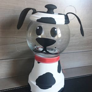 May include: A black and white painted ceramic dog-shaped candy jar with a glass jar and a red ribbon around the neck.