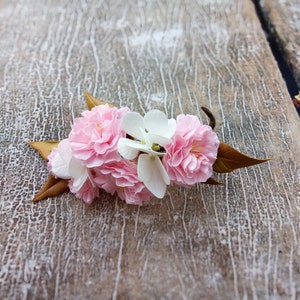 May include: A cluster of pink and white blossoms with brown leaves on a weathered wooden surface.