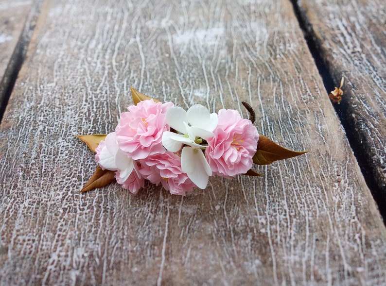 May include: A cluster of pink and white blossoms with brown leaves on a weathered wooden surface.
