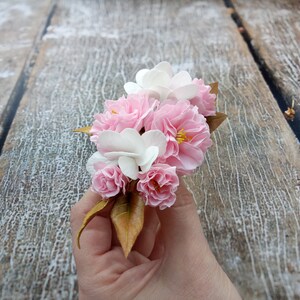 May include: A bouquet of pink and white flowers with brown leaves. The flowers are arranged in a hand.