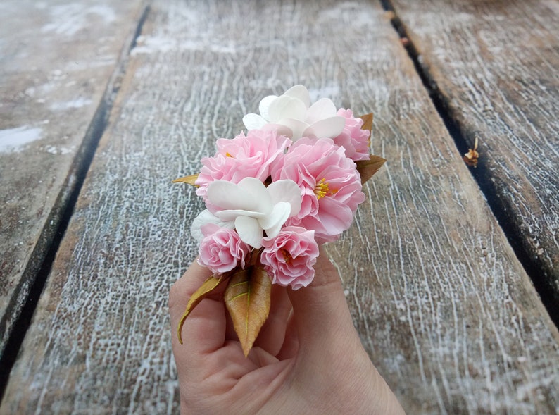 May include: A bouquet of pink and white flowers with brown leaves. The flowers are arranged in a hand.