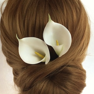 May include: Two white calla lily flower hair clips. The flowers are arranged in a simple, elegant design.