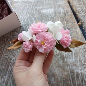 May include: A bouquet of delicate pink and white paper flowers with brown leaves. The flowers are arranged in a cluster and have a realistic appearance.