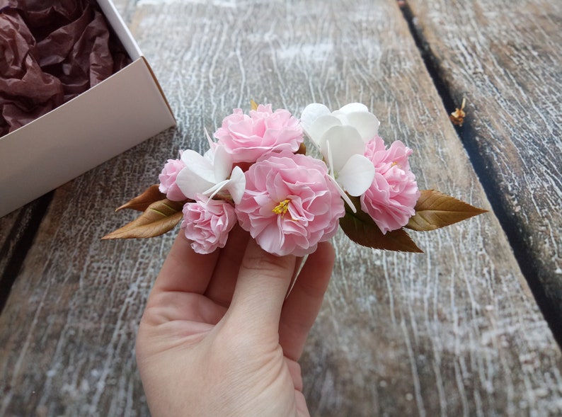 May include: A bouquet of delicate pink and white paper flowers with brown leaves. The flowers are arranged in a cluster and have a realistic appearance.