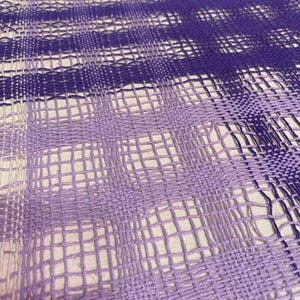 Puede incluir: Primer plano de una tela tejida con un degradado de morado y blanco. La tela está tejida en un patrón de cuadrícula, creando una superficie texturizada.