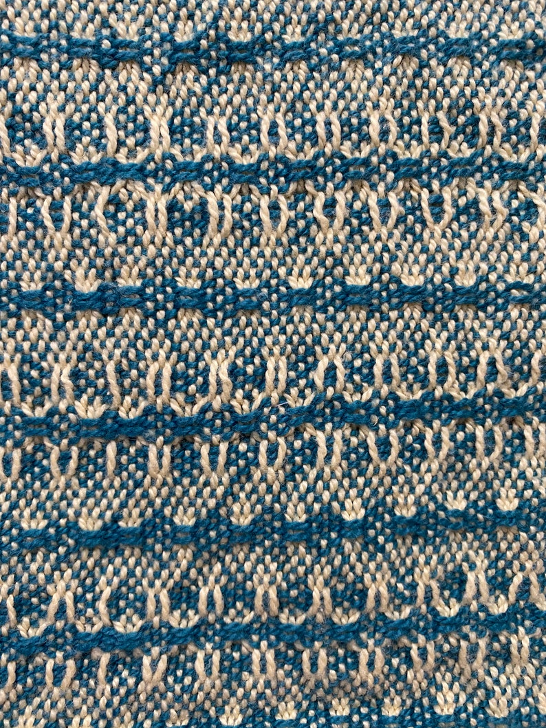 May include: Close-up of a woven fabric with a repeating pattern of white and blue. The fabric has a textured surface and a subtle sheen.