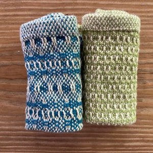 May include: Two small, rolled-up dishcloths. One is blue and white with a geometric pattern, the other is green and white with a woven pattern.
