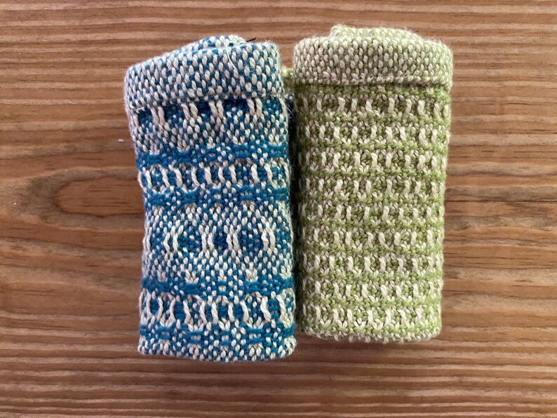 May include: Two small, rolled-up dishcloths. One is blue and white with a geometric pattern, the other is green and white with a woven pattern.