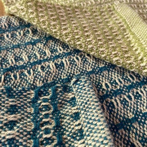 May include: Two woven kitchen towels, one in a light green and white pattern and the other in a blue and white pattern.
