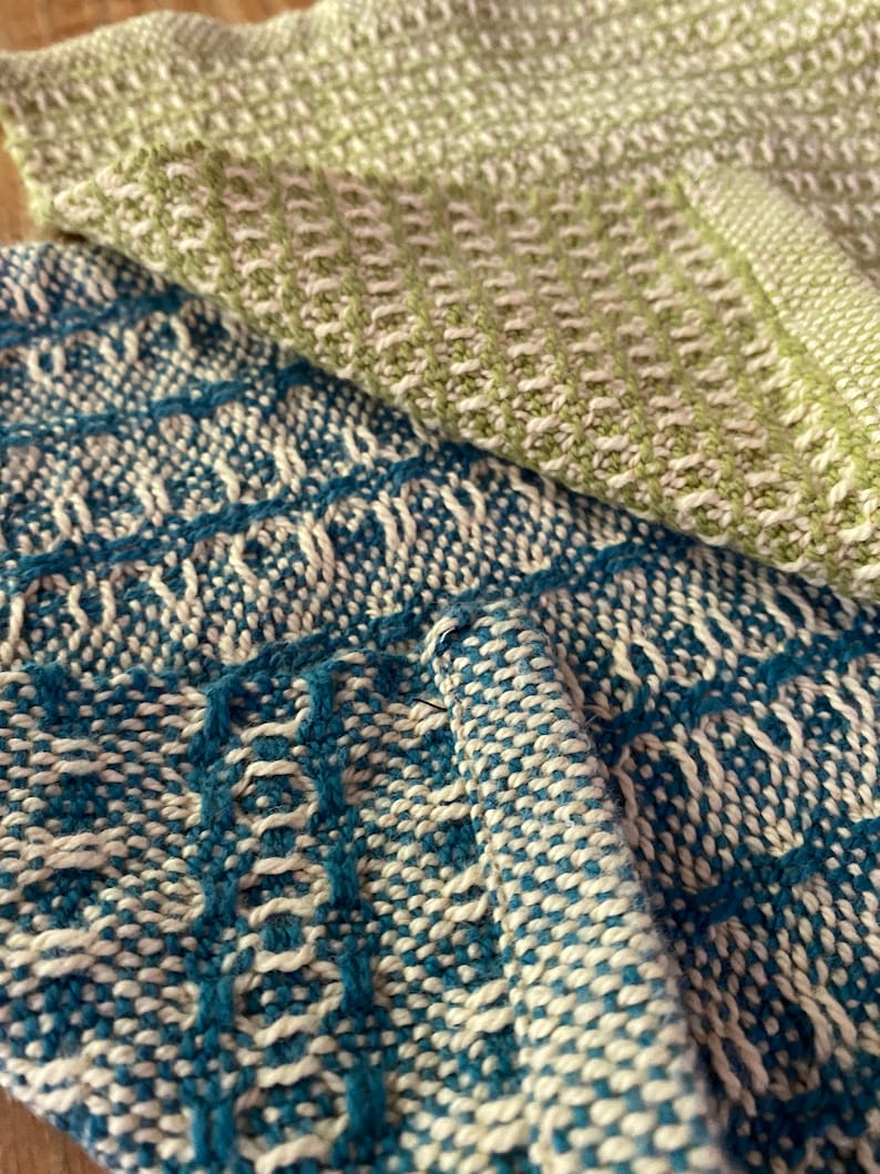 May include: Two woven kitchen towels, one in a light green and white pattern and the other in a blue and white pattern.