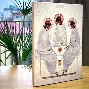 May include: A white wooden plaque with a religious icon depicting three figures in white robes with halos. The icon is titled "Holy Trinity" in black text.