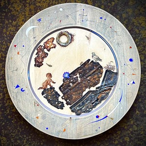 May include: A circular wooden decorative plate featuring mixed media elements including a small metal ring, a silhouette of a crawling figure, a textured rusted metal piece, and a pigeon perched on a dark, weathered, rectangular metal fragment.
