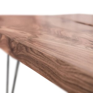 May include: Close-up of a wooden table top with a natural edge and a dark brown wood grain. The table has black hairpin legs.