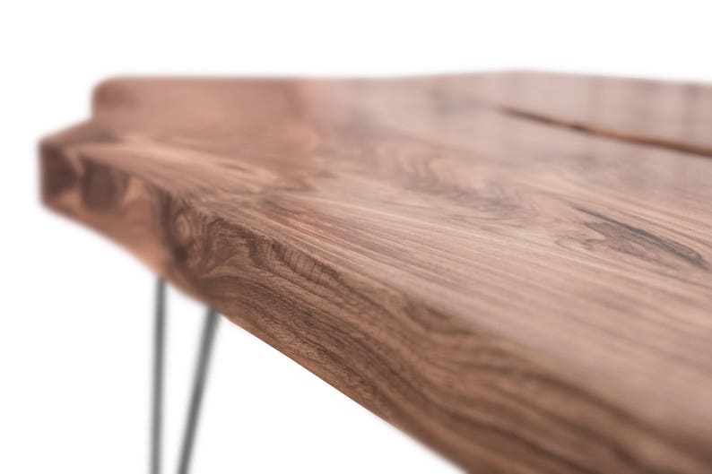 May include: Close-up of a wooden table top with a natural edge and a dark brown wood grain. The table has black hairpin legs.
