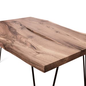 May include: A rustic wooden table with a live edge top and black hairpin legs. The table has a natural wood finish and a unique grain pattern.