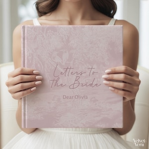 Può includere: Un libro rosa chiaro intitolato "Letters to the Bride" con il nome "Dear Olivia" sotto. Il libro ha un design decorativo ed è tenuto da una persona che indossa un vestito bianco.