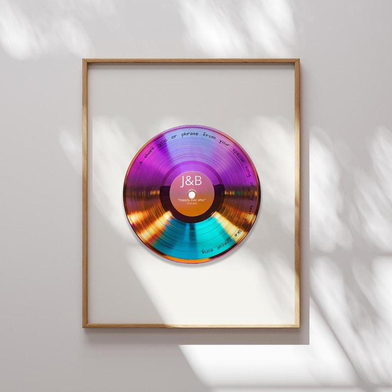 May include: A framed wall art print featuring a circular, iridescent vinyl record graphic with a central label displaying the letters J&B and the text "happily ever after". The record surface includes handwritten text along the outer edge.