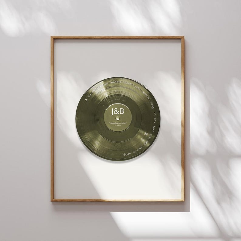May include: A framed wall art piece featuring a translucent olive green vinyl record. The center label displays the letters J&B and the text Happily ever after. Handwritten white text circles the record, reading A short phrase, special song or any text you like special song.